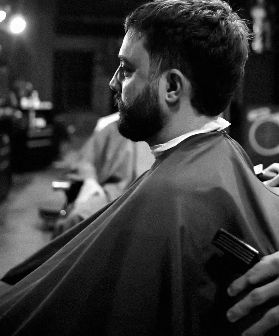 Cliente de barba na cadeira, de capa, durante o corte